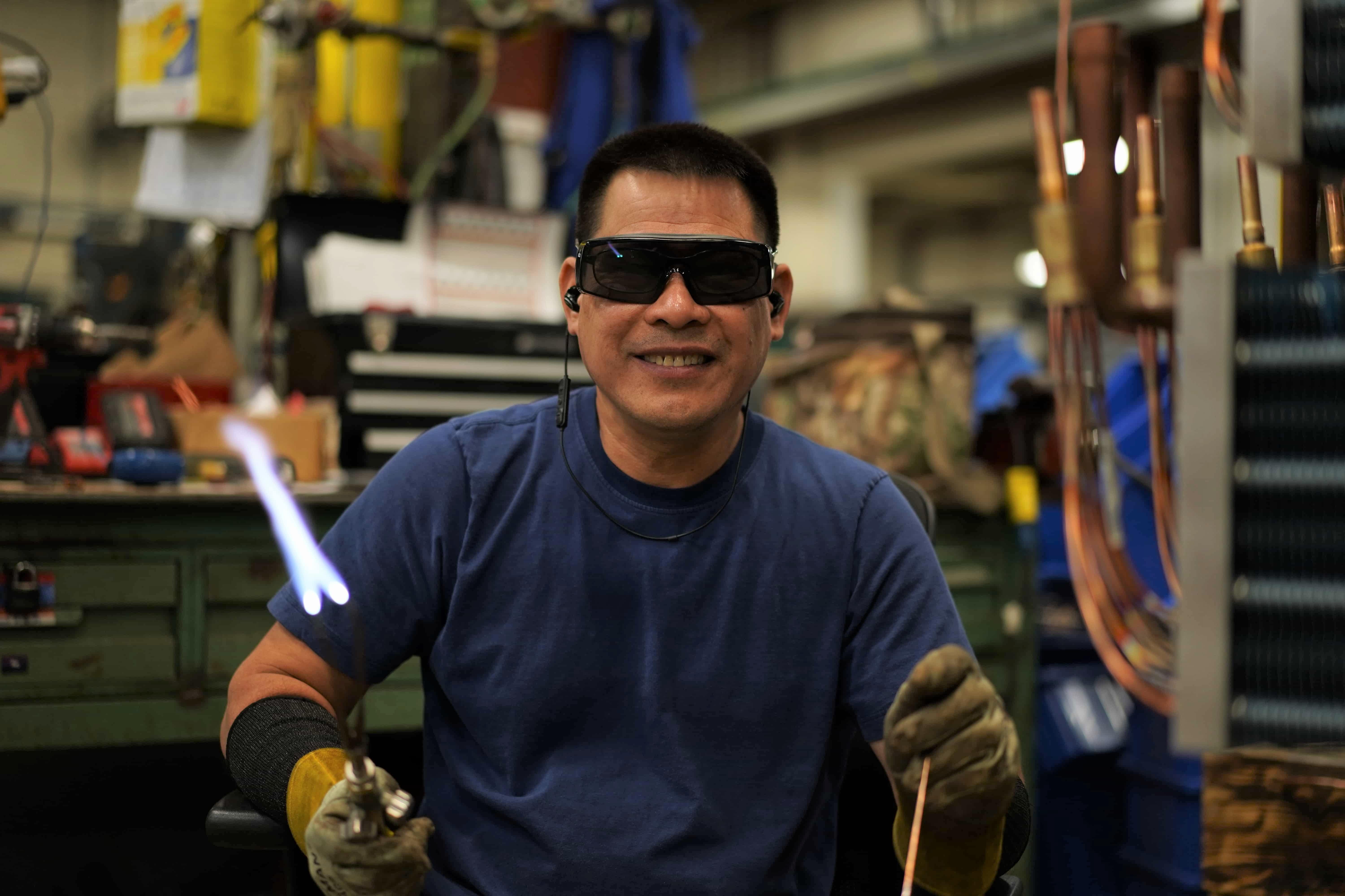brazer smiling and holding lit torch in factory setting