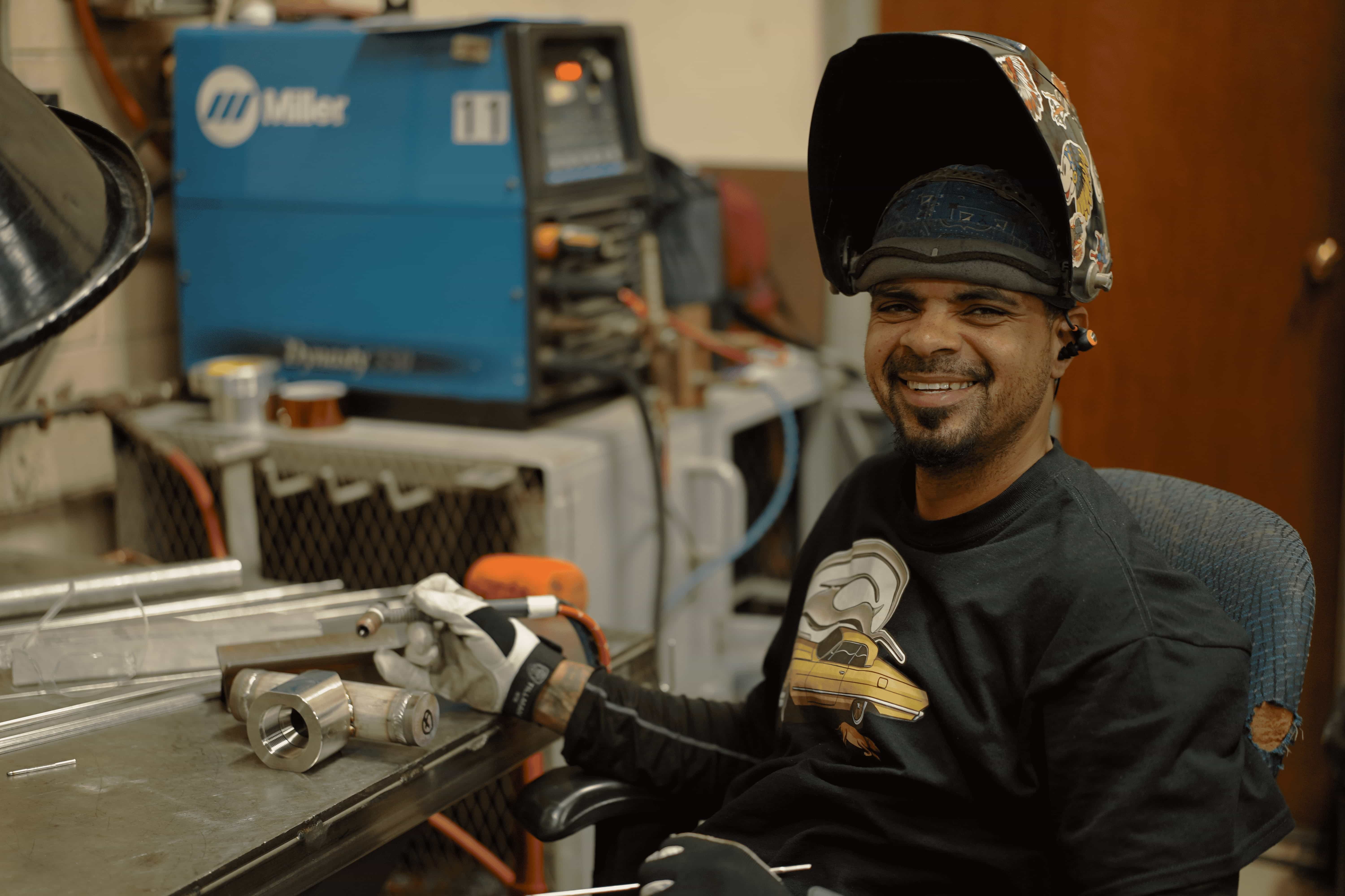 male welder smiling at camera with helmet on