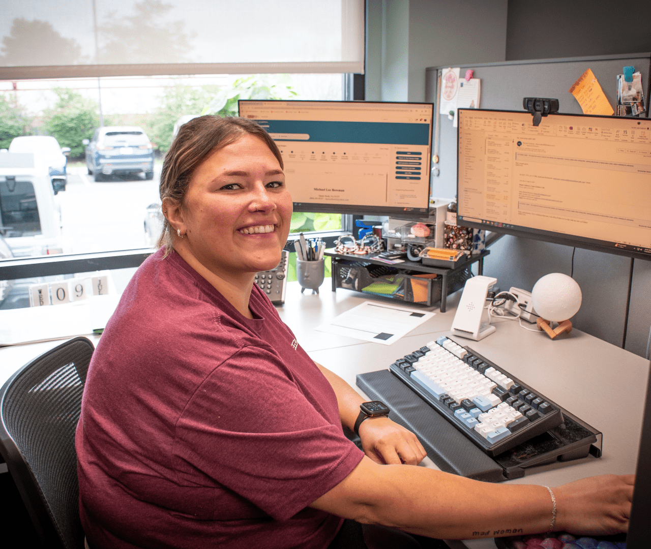 woman in maroon seated at computer and smiling for camera